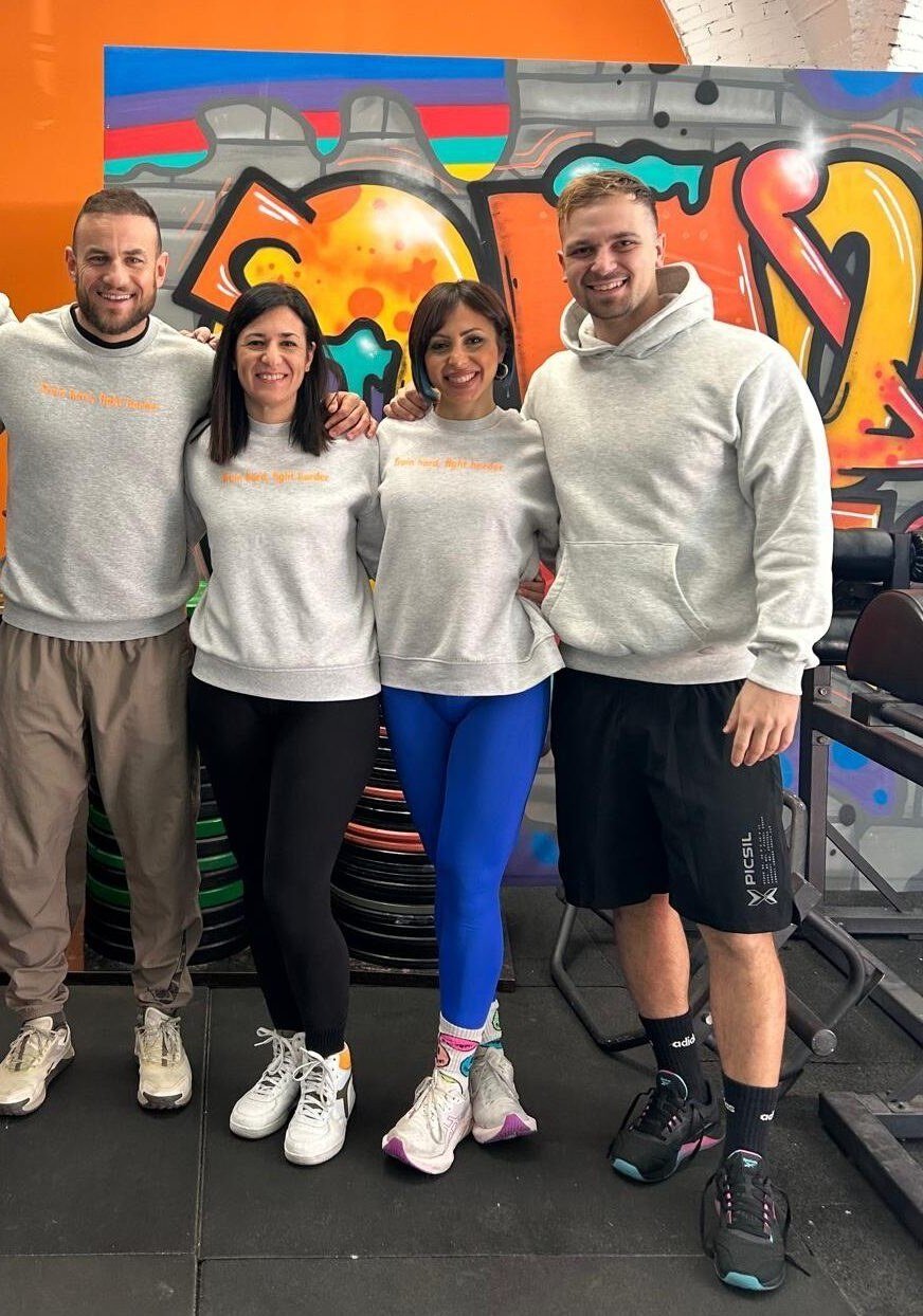 Lo staff OFIT, quattro persone in felpa grigia davanti al murale colorato del box